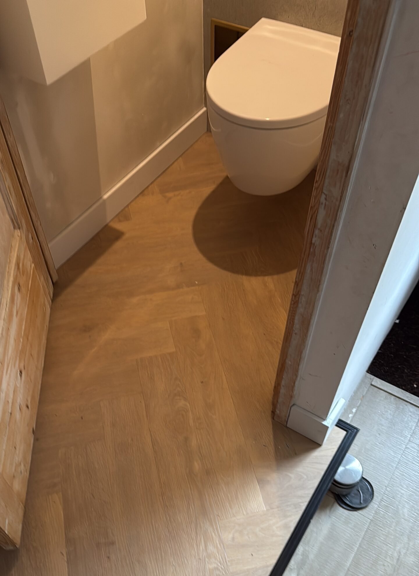 Toilet ruimte met lichtbruine visgraat vloer en witte wc pot.